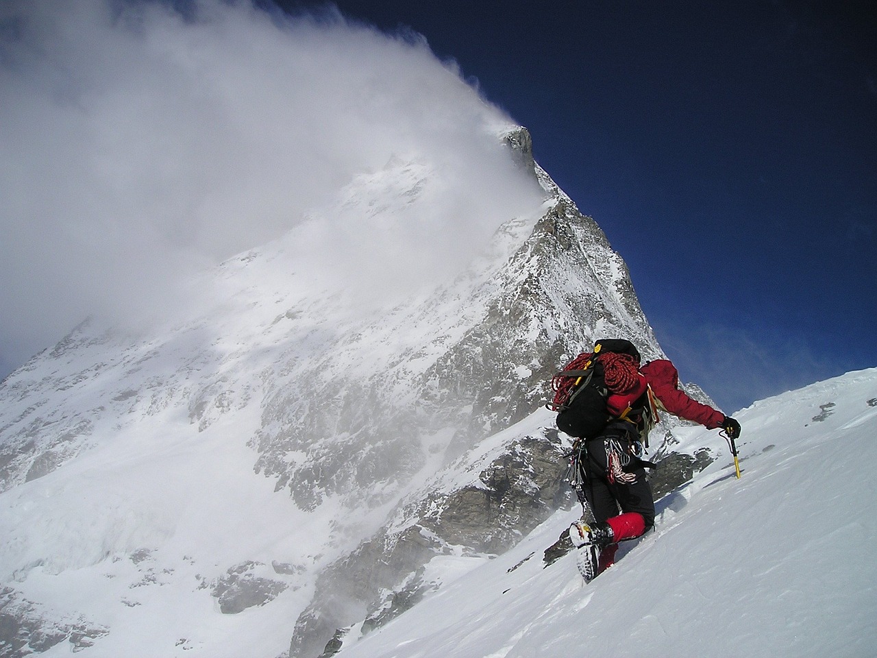 Climber on a narrow alpine ridge in storm wind and snow